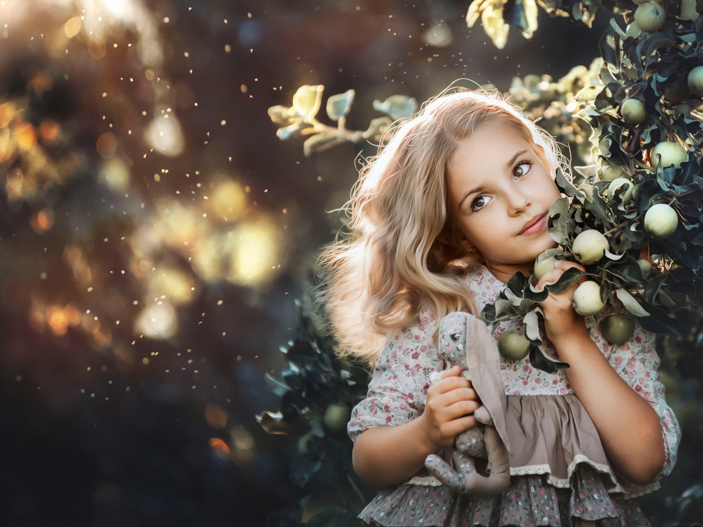 Маленькая девочка стоит у ветки с яблоками