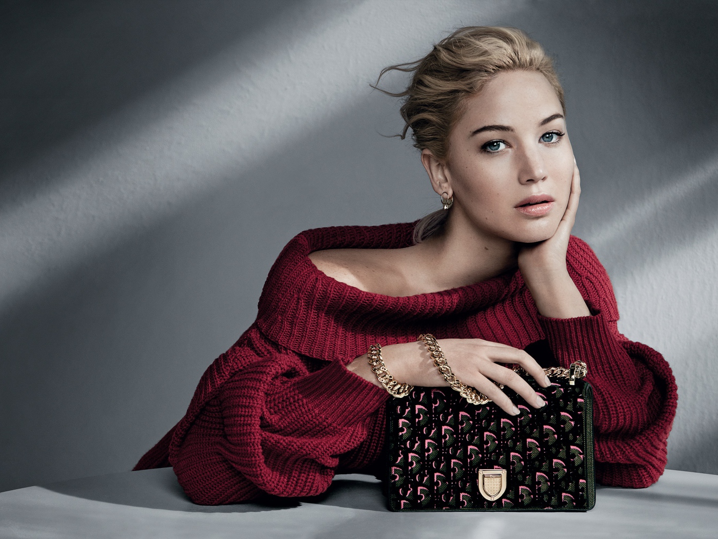 Актриса Дженнифер Лоуренс в красном свитере с сумочкой на сером фоне