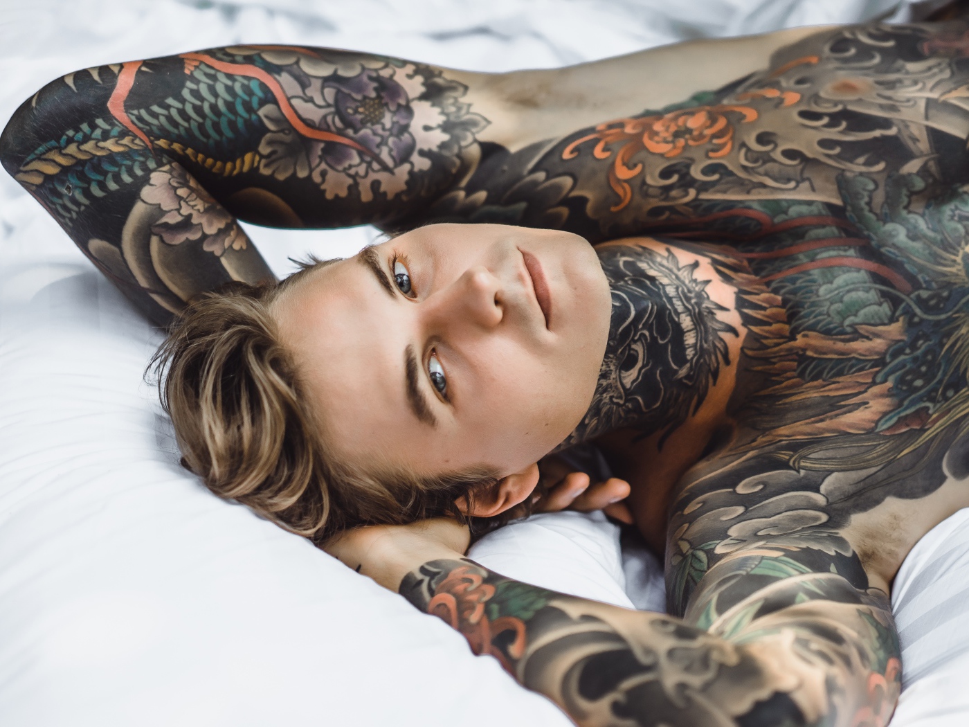 Красивый молодой человек с татуировками на теле лежит на кровати