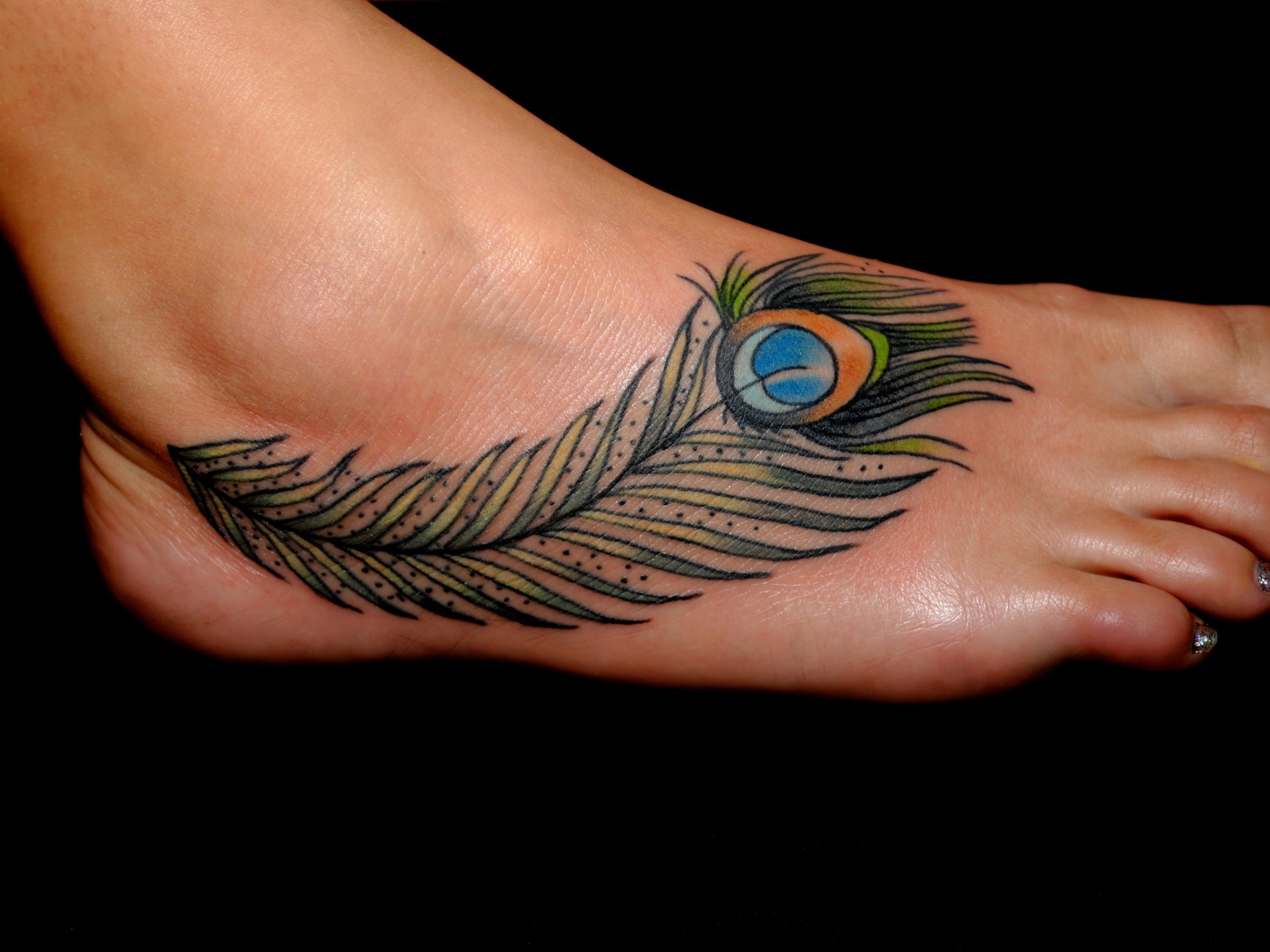 Peacock feather tattoo on leg on black background