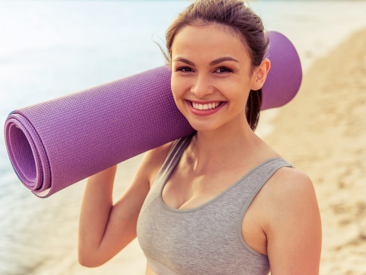 Спортивная девушка с ковриком для йоги на пляже