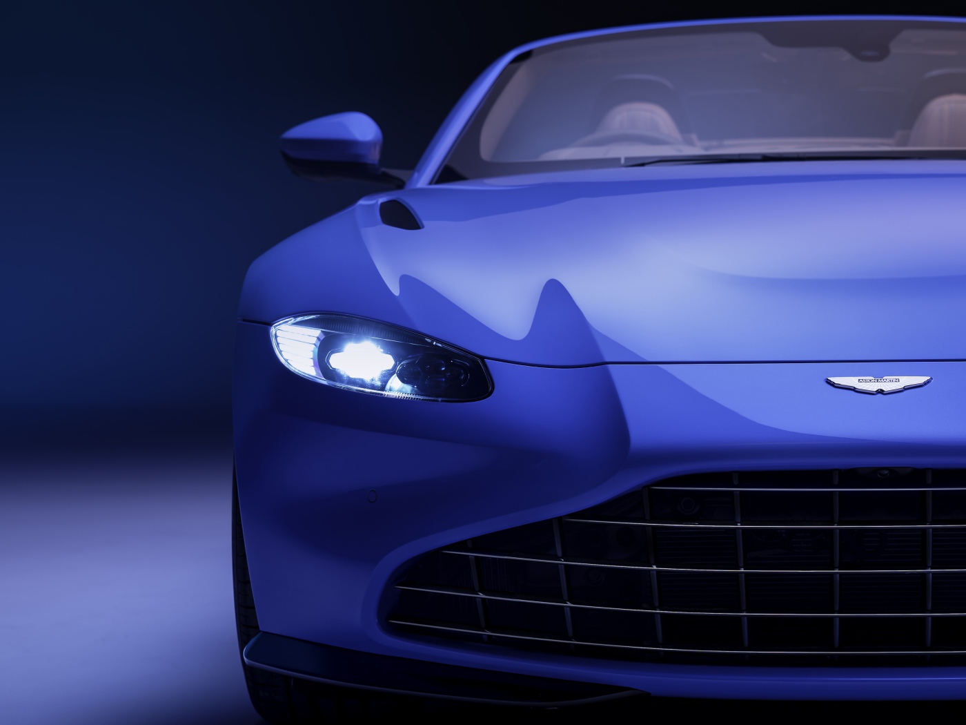 Синий автомобиль Aston Martin Vantage Roadster 2020 года с включенной фарой 