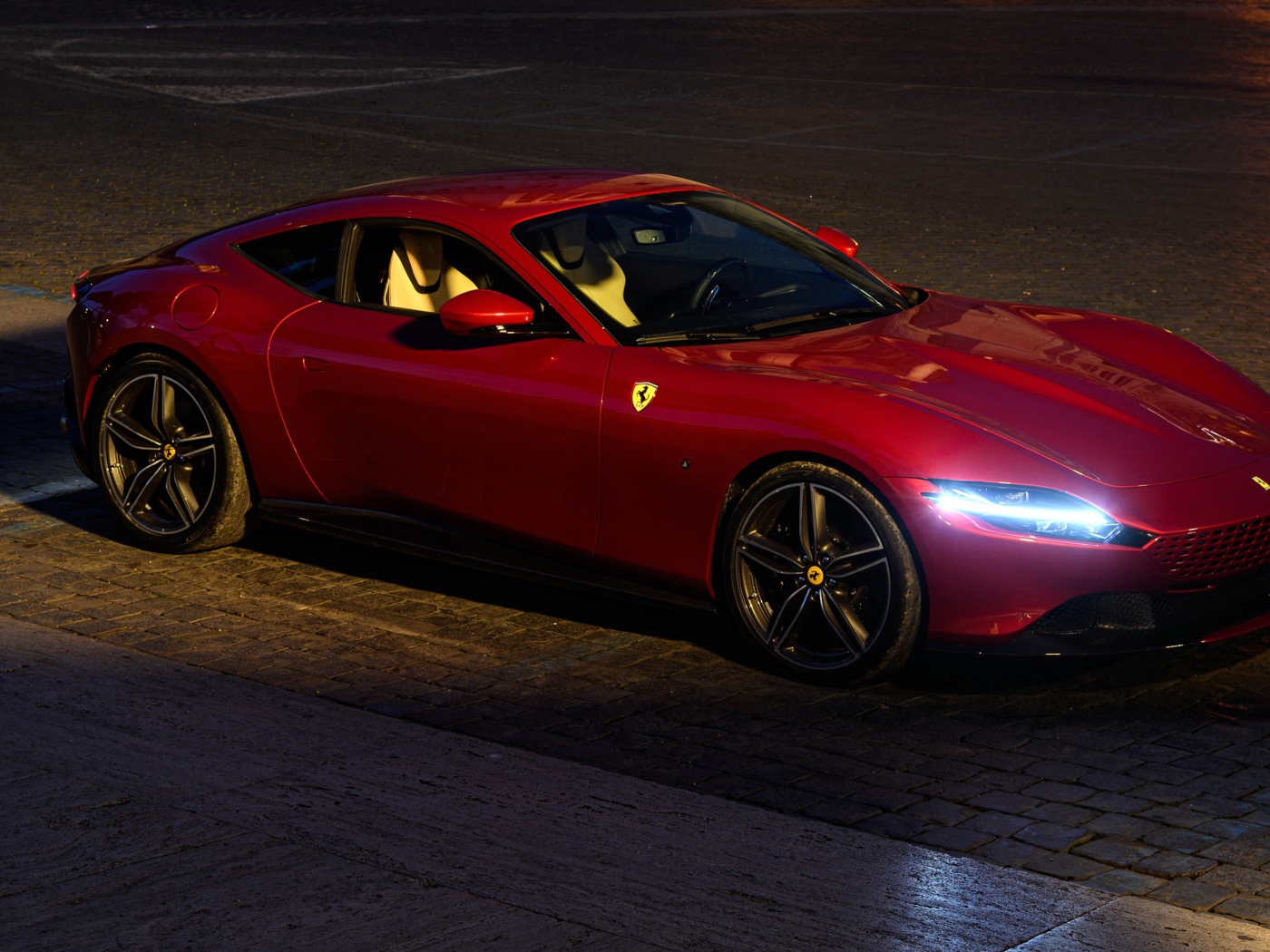 Красный автомобиль Ferrari Roma 2020 года с включенными фарами вечером
