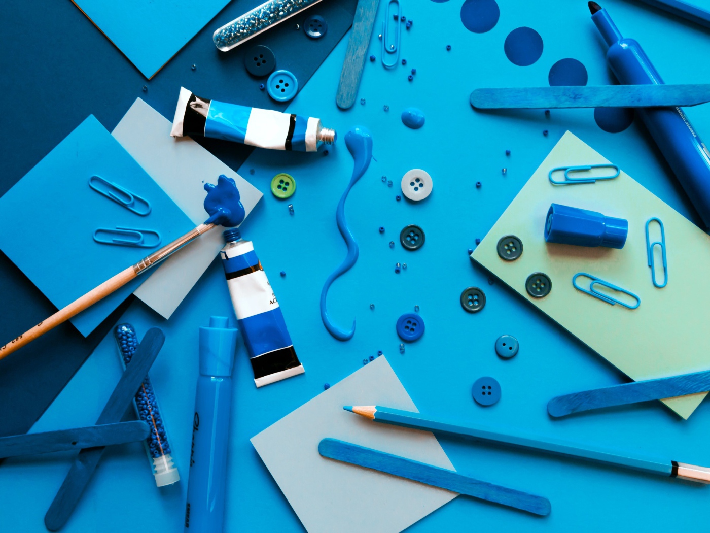 Синие краски и канцелярские предметы на столе с бумагой 