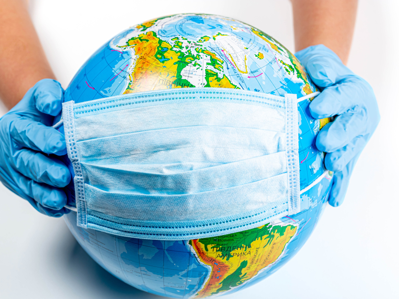 Руки одевают маску от коронавируса на глобус 