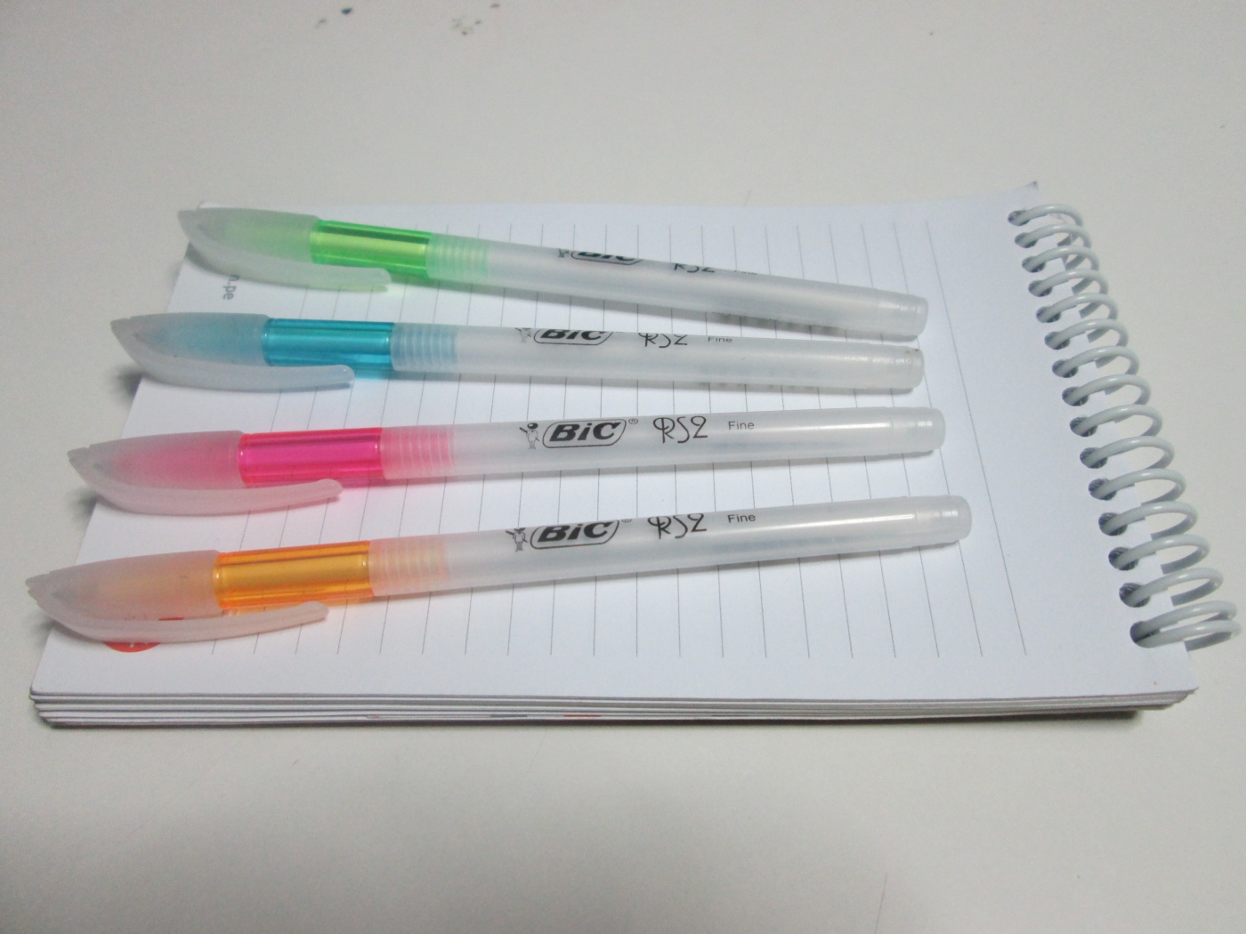 Разноцветные ручки лежат на блокноте на белом фоне 