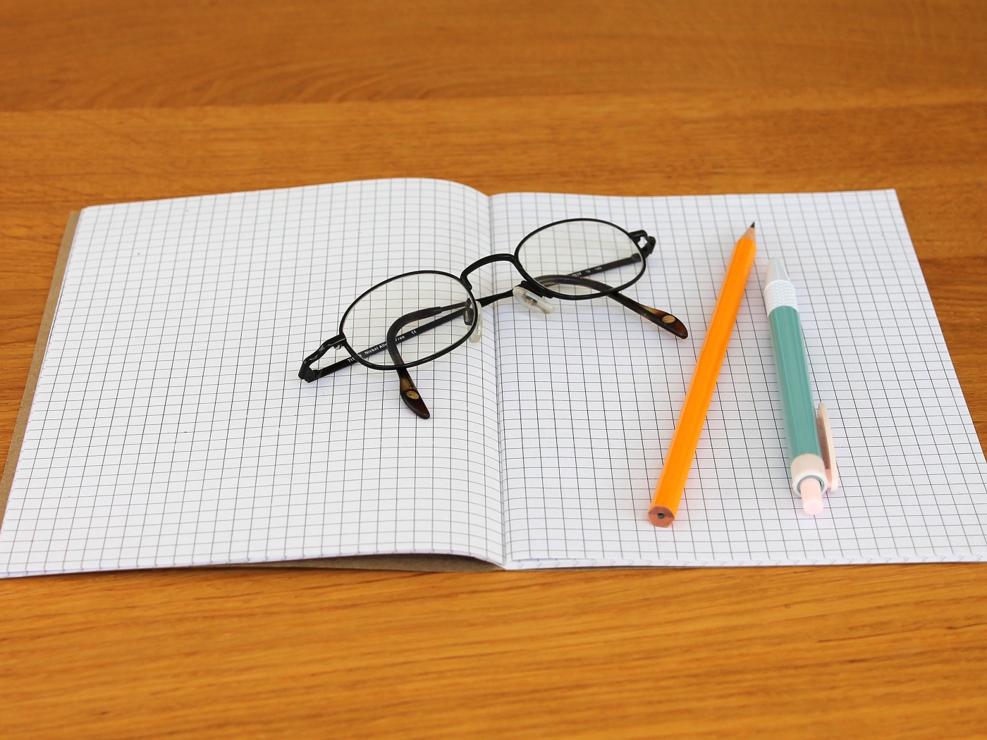 Тетрадь, ручка, карандаш и очки лежат на парте