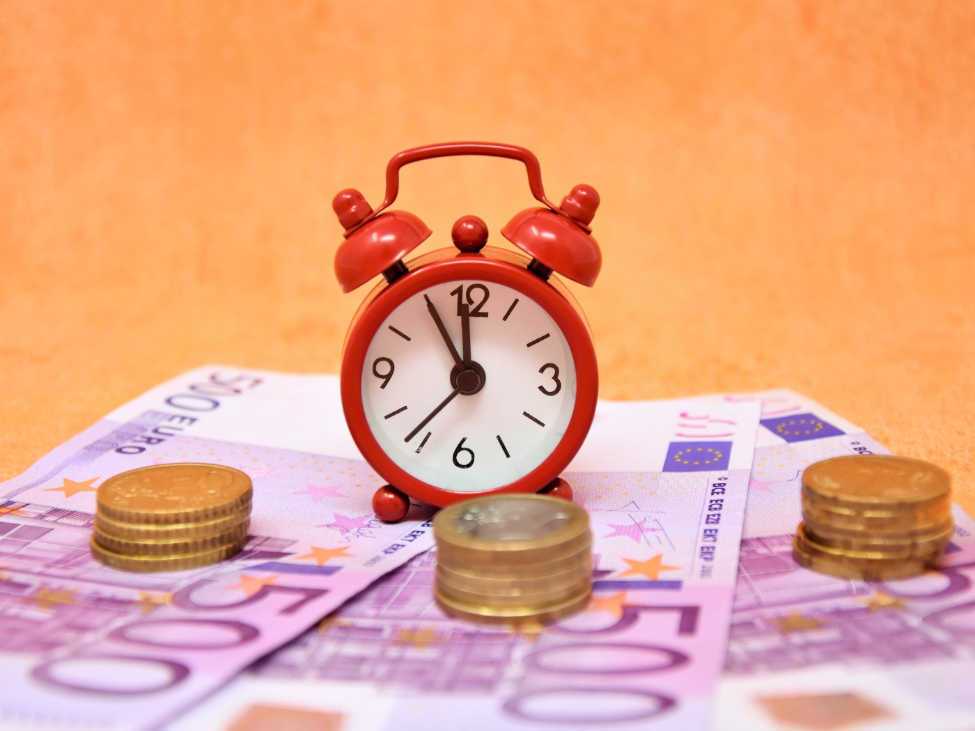 Маленький красный будильник с купюрами евро и монетами