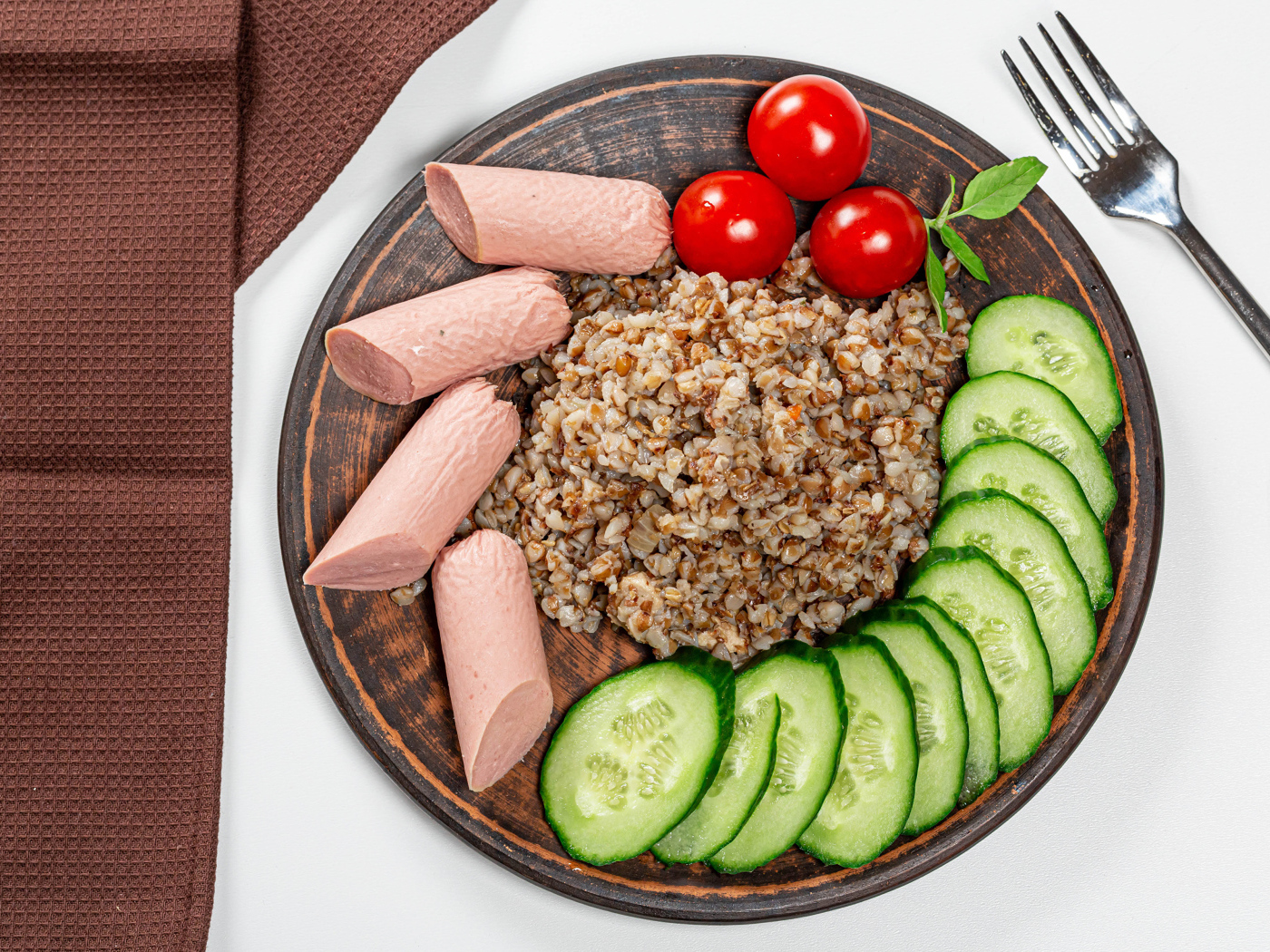 Гречка на тарелке с помидорами, огурцами и сосисками