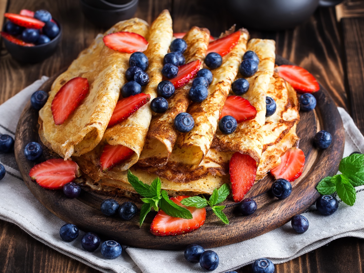 Вкусные тонкие блинчики на деревянной доске с ягодами черники и клубники 