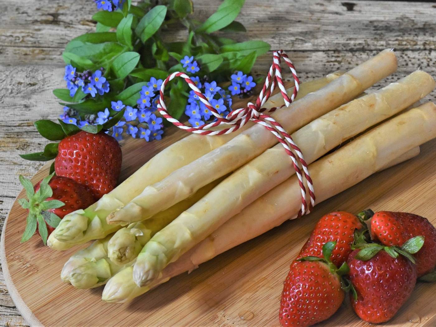 Fresh asparagus on the table with strawberries and forget-me-not flowers