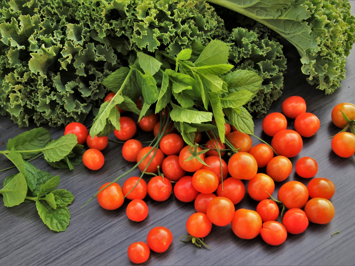 Красные мелкие помидоры на столе с зеленью 