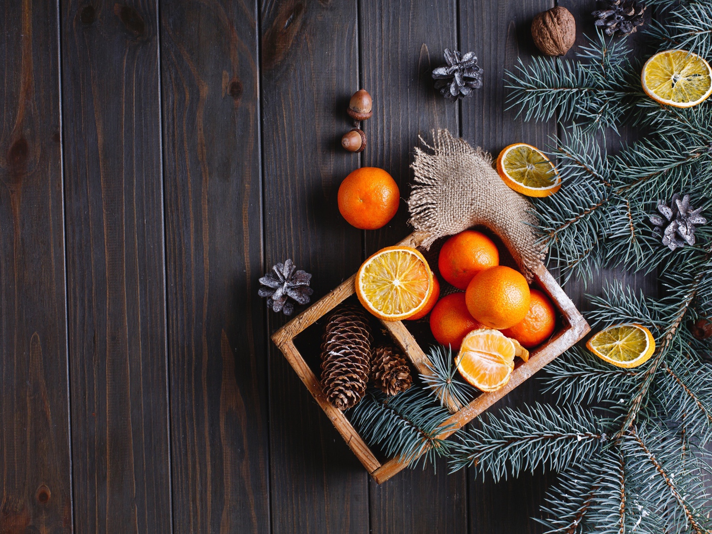 Ящик с мандаринами и шишками на столе с еловыми ветками