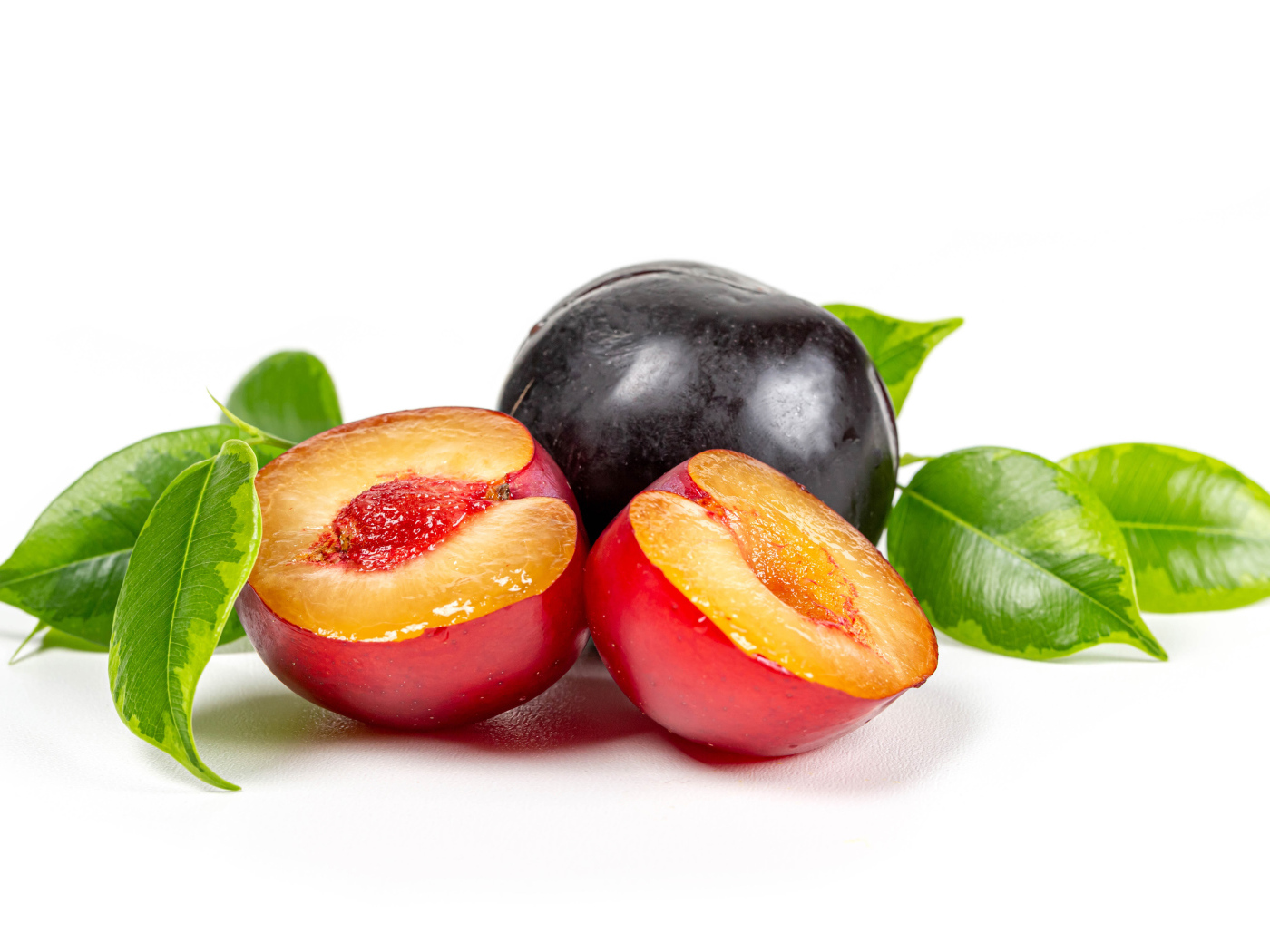 Сочные аппетитные сливы на белом фоне с зелеными листьями