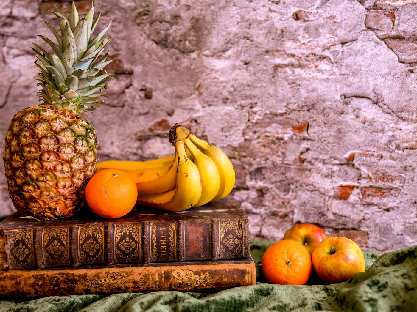 Ананас, бананы, апельсин и яблоки лежат на столе с книгами