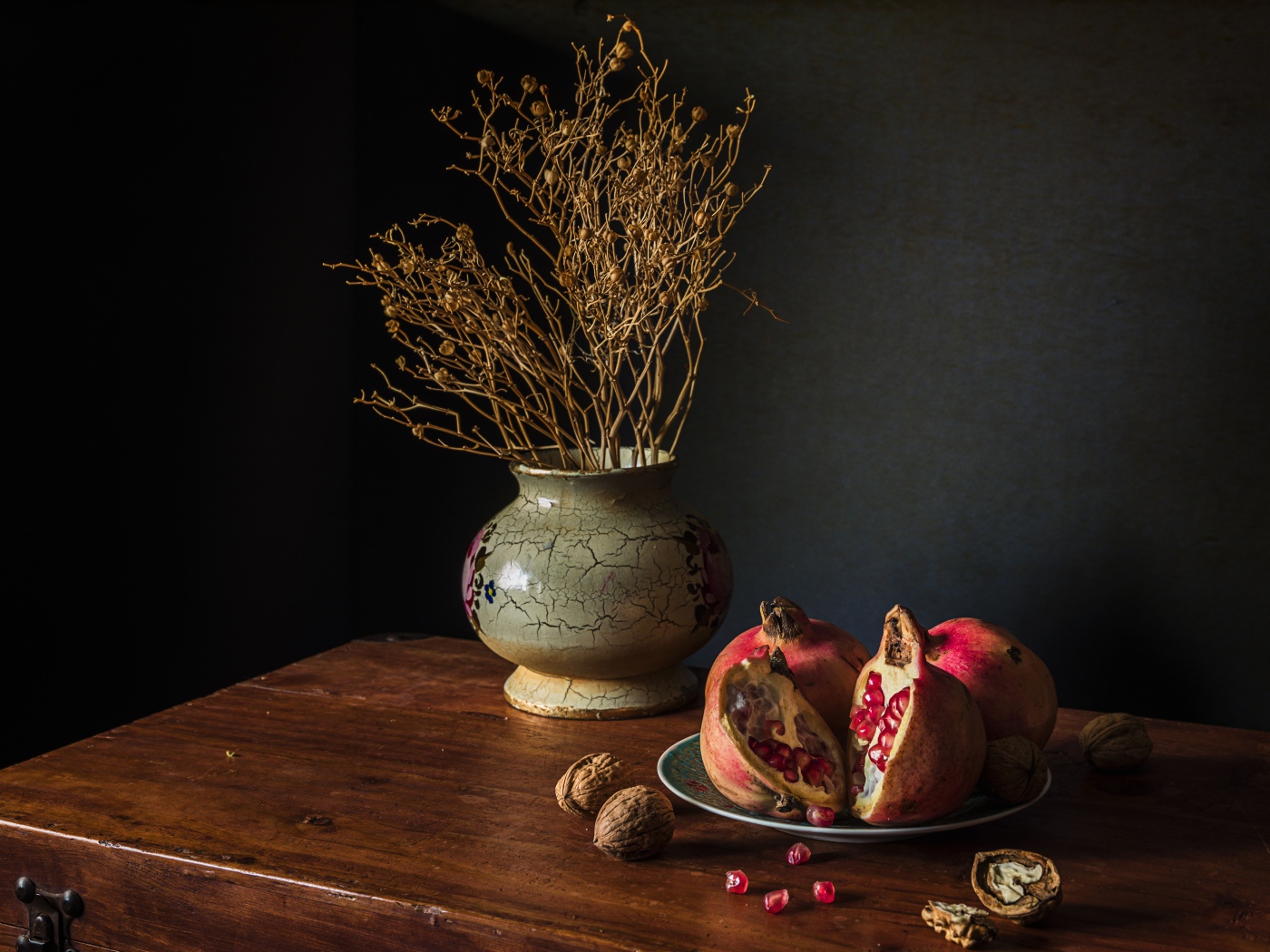Красный гранат на столе с грецкими орехами и сухой веткой в вазе