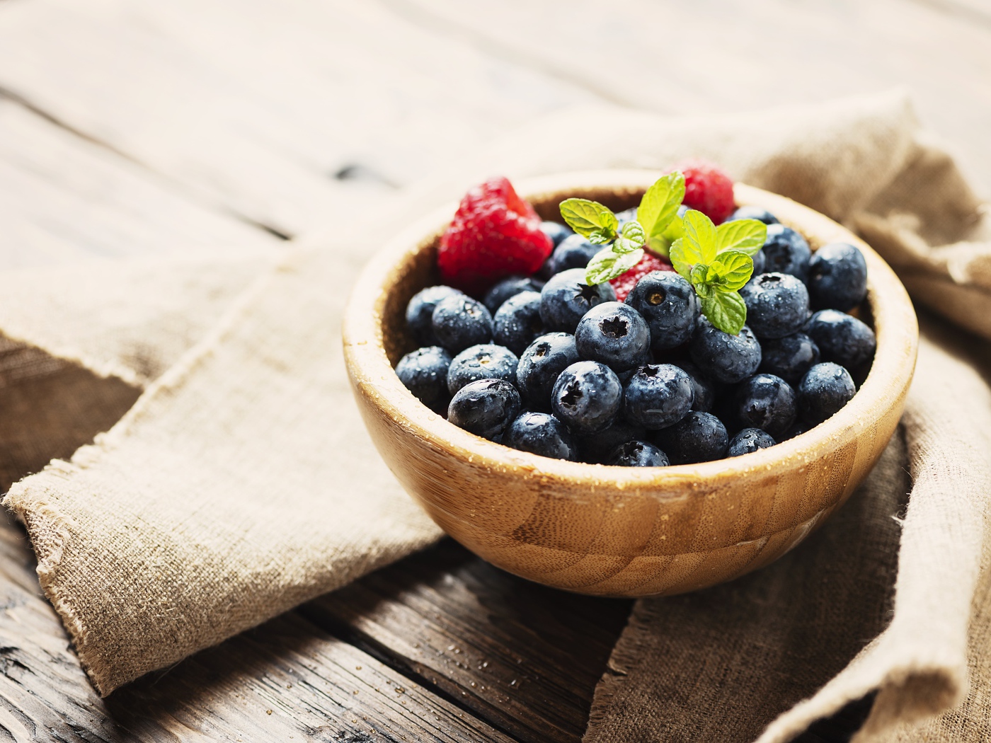 Мокрые ягоды черники в деревянной миске с малиной 