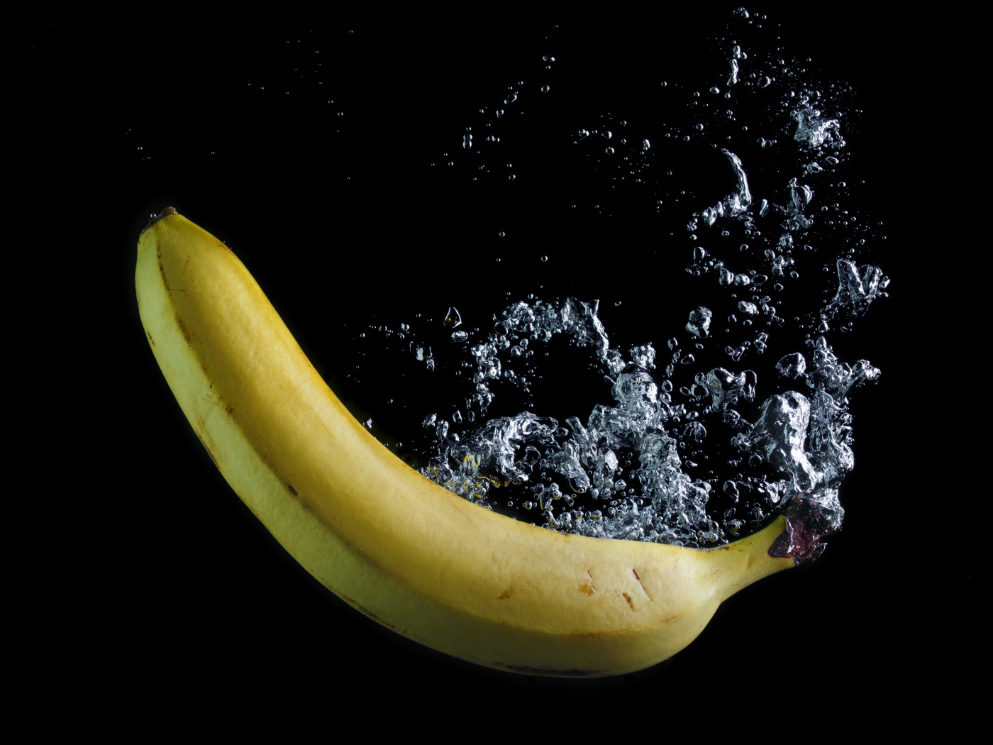 Желтый банан в воде на черном фоне