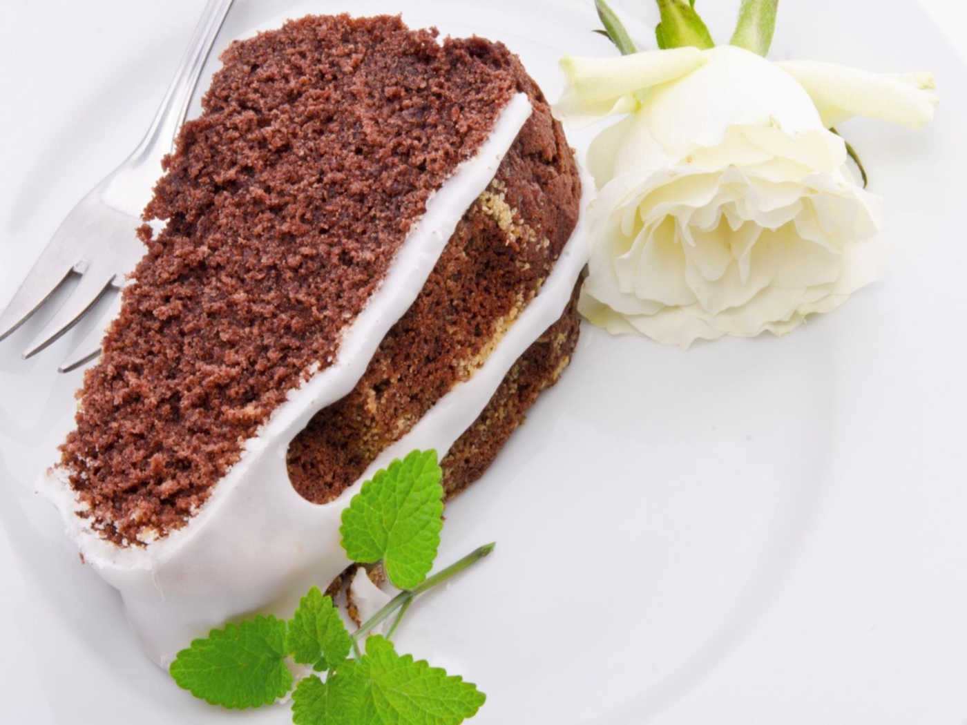 Кусок шоколадного пирога на тарелке с белой розой 