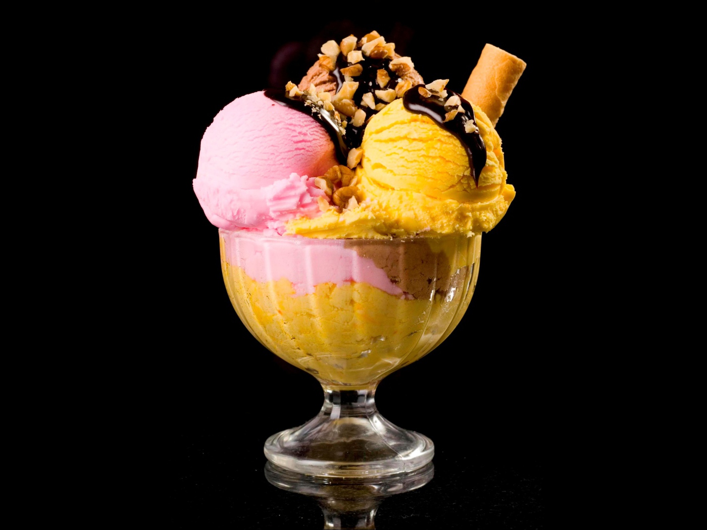 Шарики фруктового мороженого в креманке с орехами и шоколадом на черном фоне