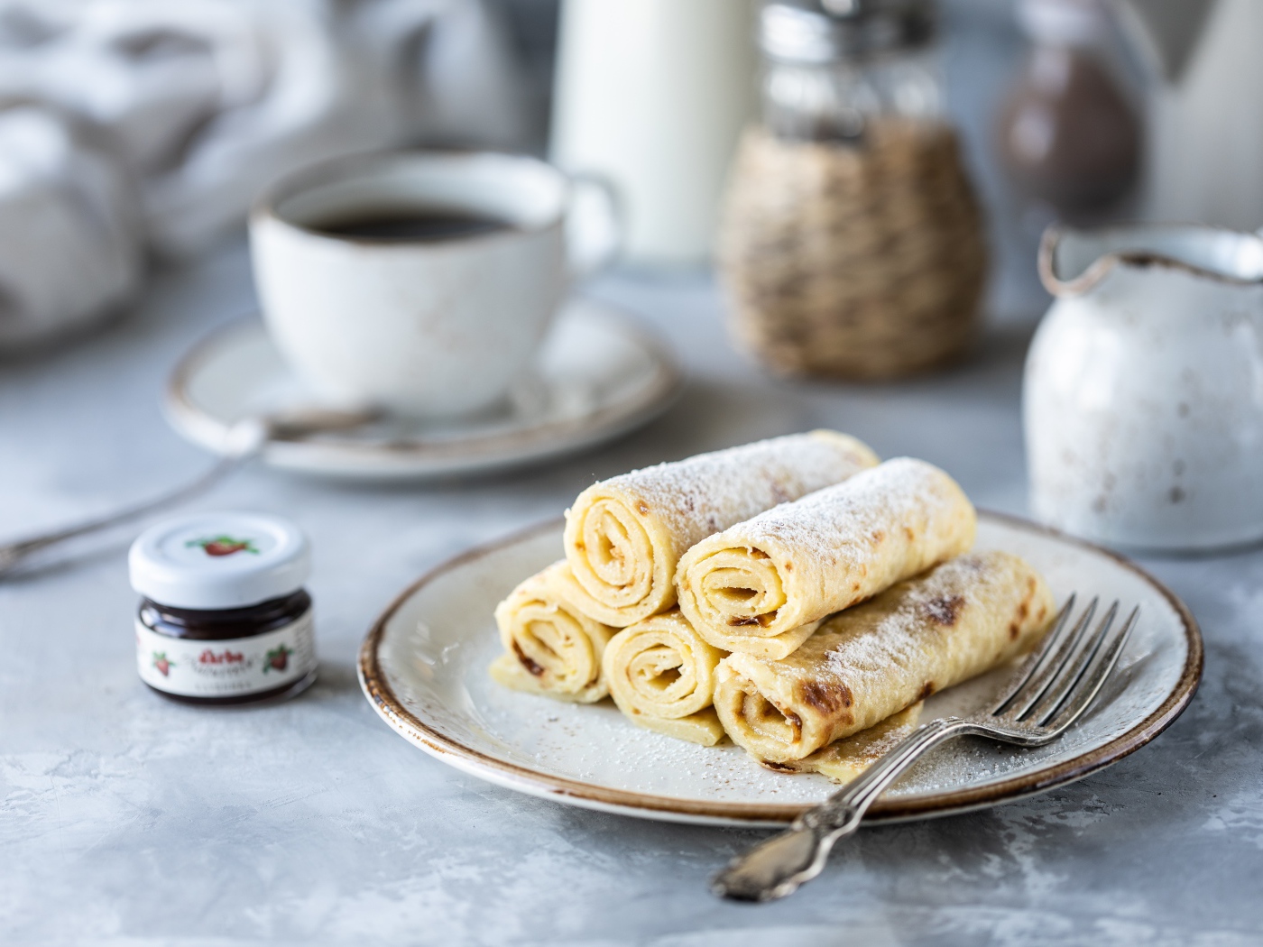 Блины на тарелке с сахарной пудрой на столе с кофе