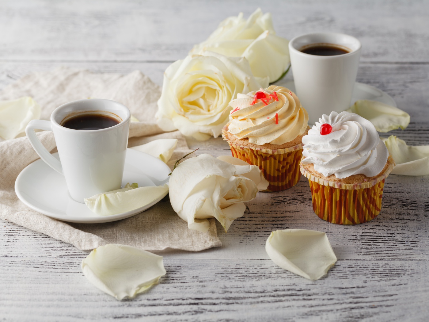 Две чашки кофе на столе с белыми розами и кексами