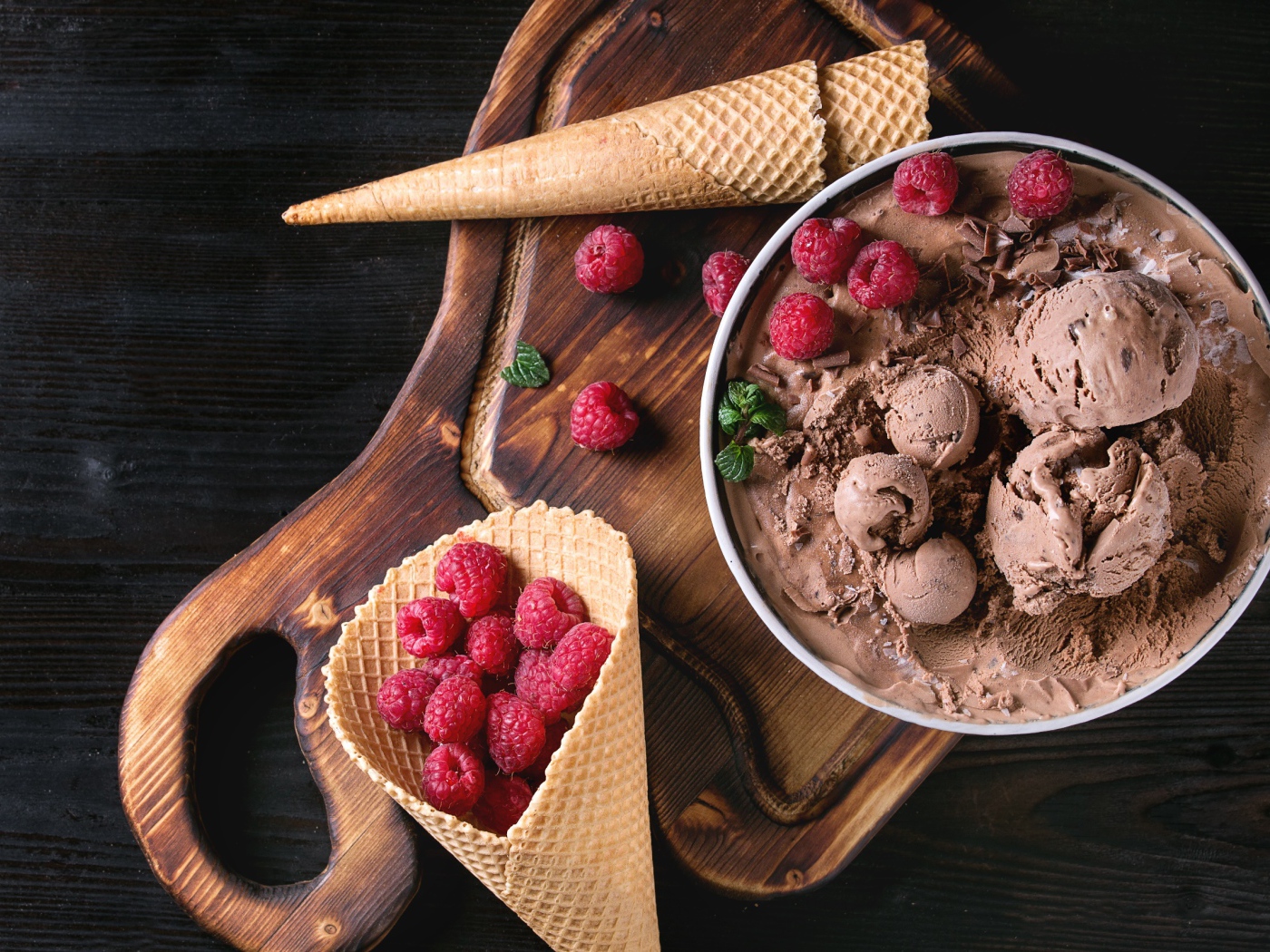 Вафельный рожок с шоколадным мороженым и ягодами малины на столе