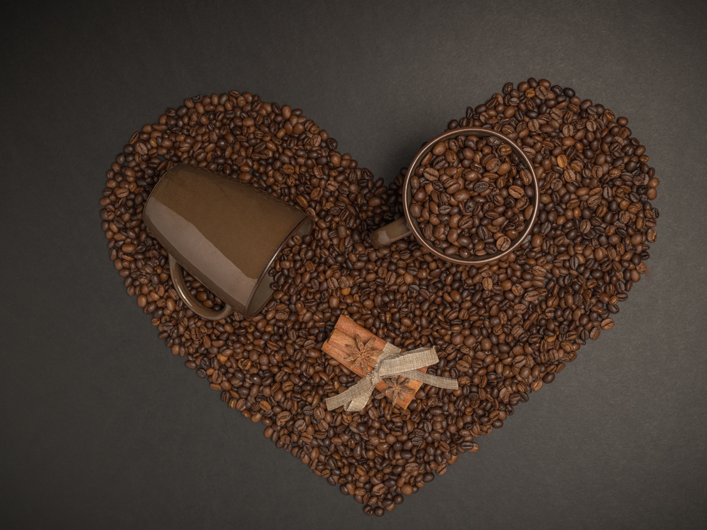Сердце из кофейных зерен на сером фоне с кружками 