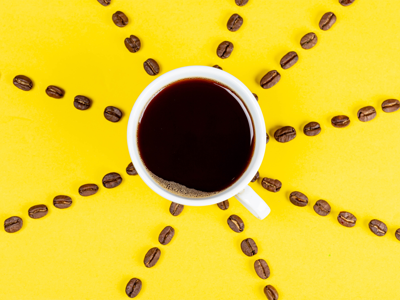 Солнце из чашки кофе с зернами на желтом фоне