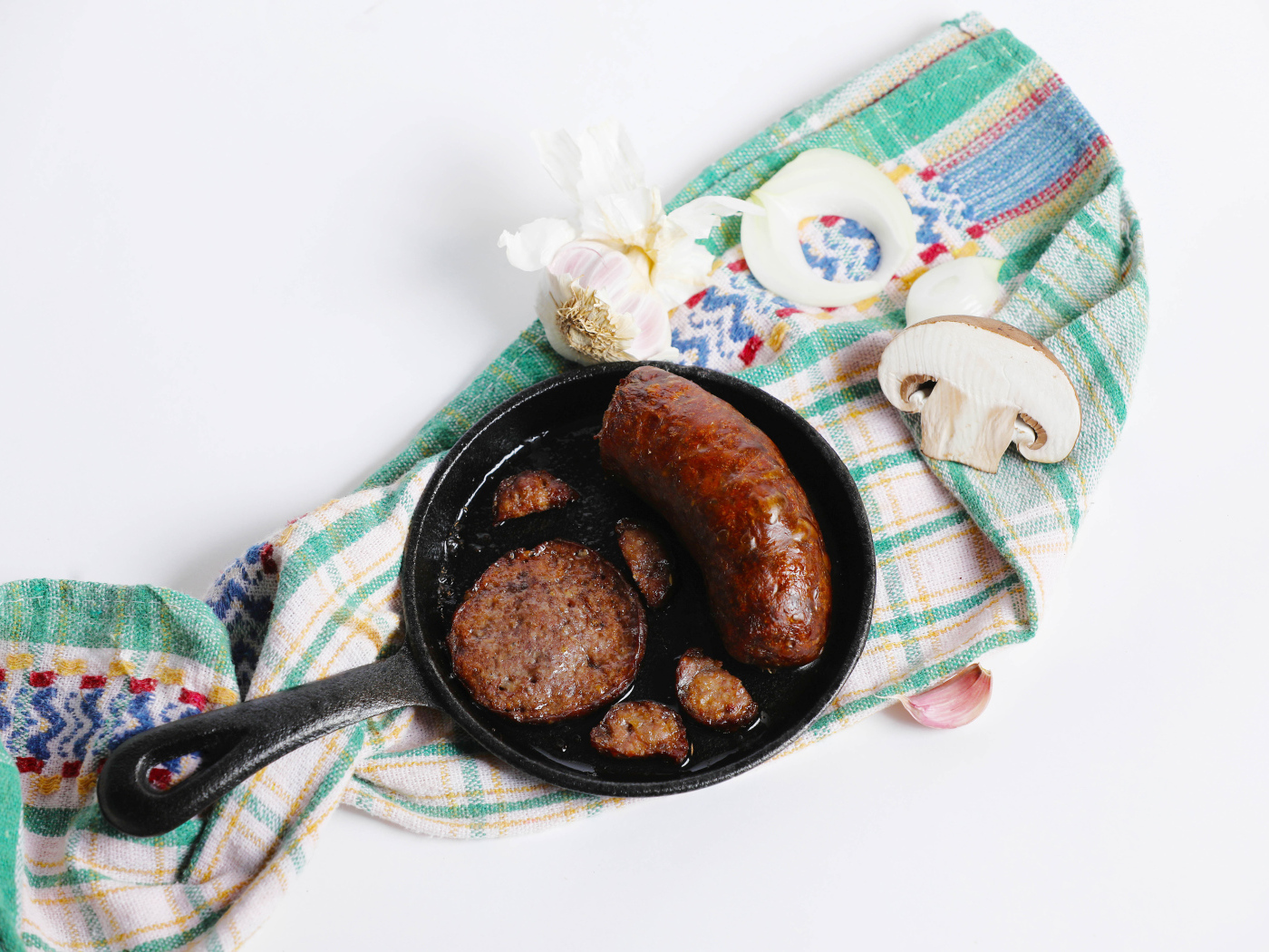 Сковорода с жареной колбасой на столе с полотенцем и чесноком