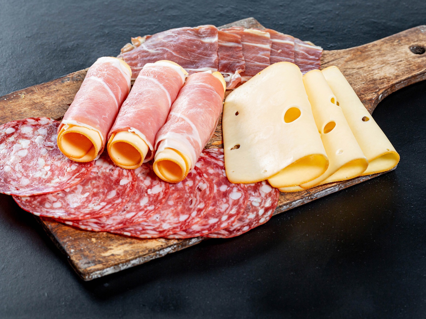 Куски сыра, ветчины и колбасы на доске