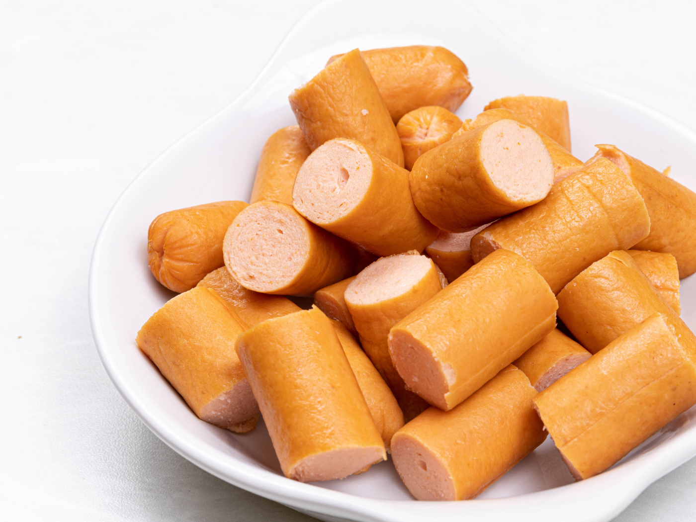 Молочные сосиски кусочками на белом фоне