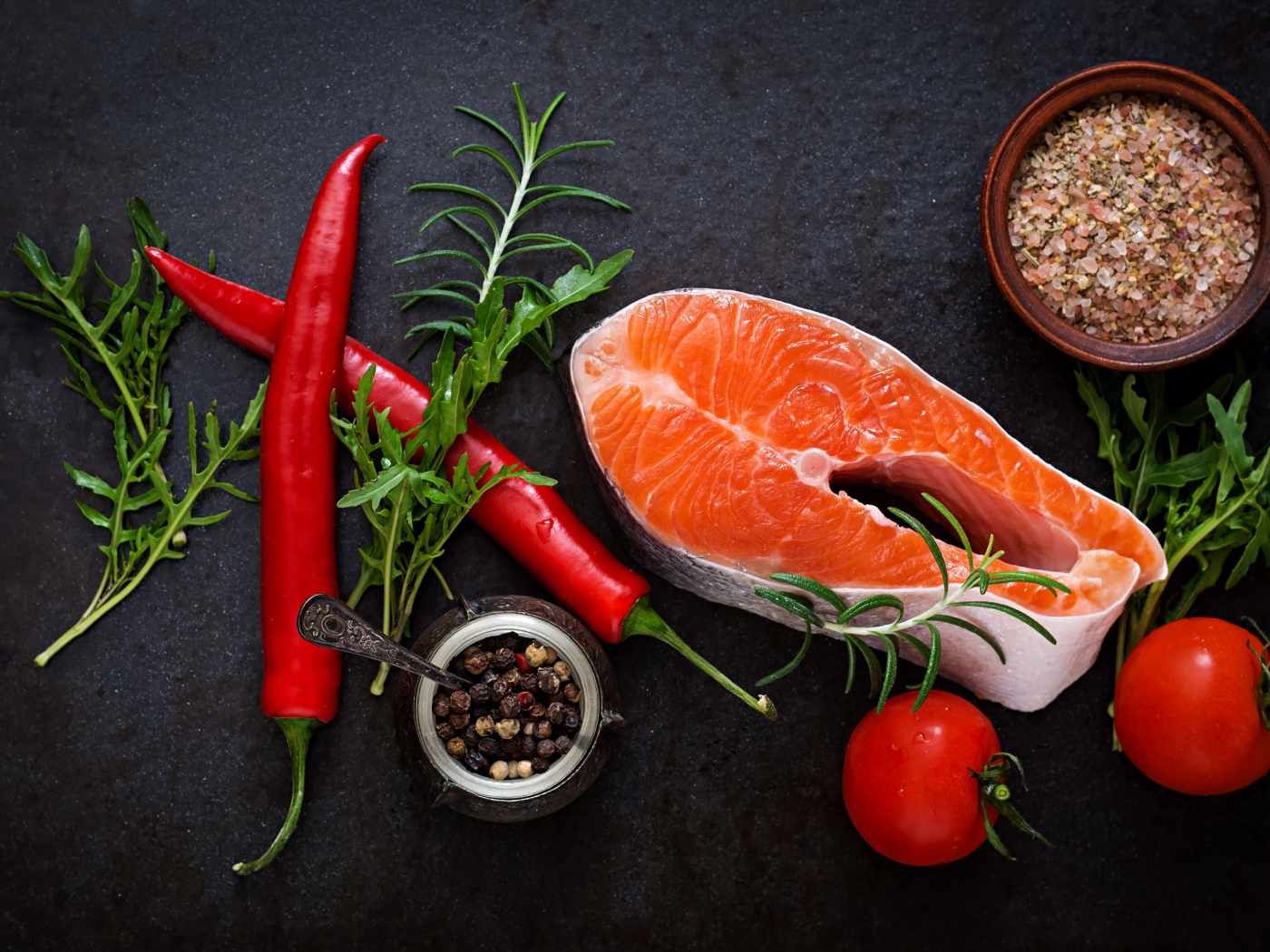 Кусок свежей красной рыбы на столе со специями, красным перцем и помидорами