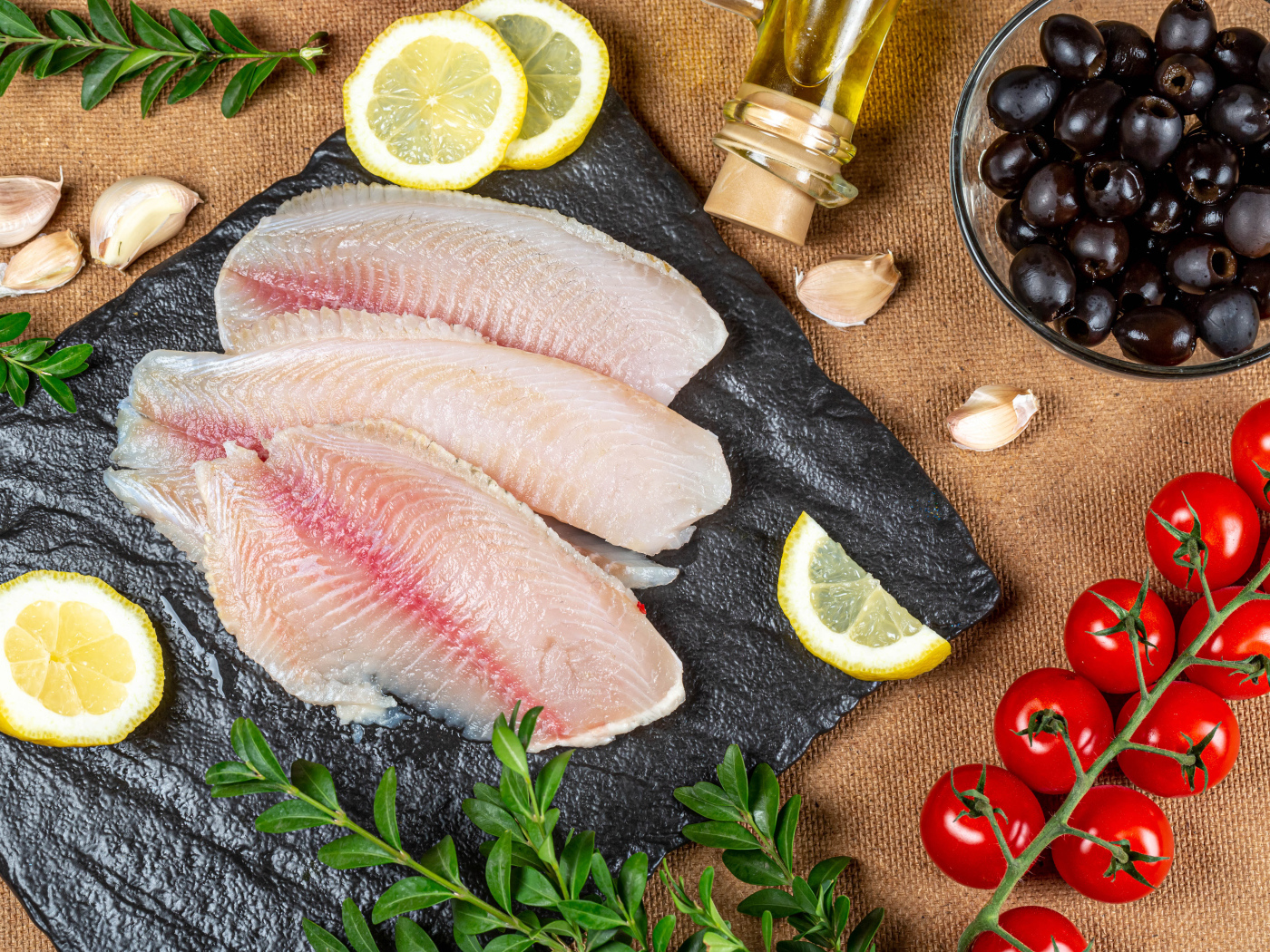 Филе рыбы на столе с лимоном, помидорами и оливками