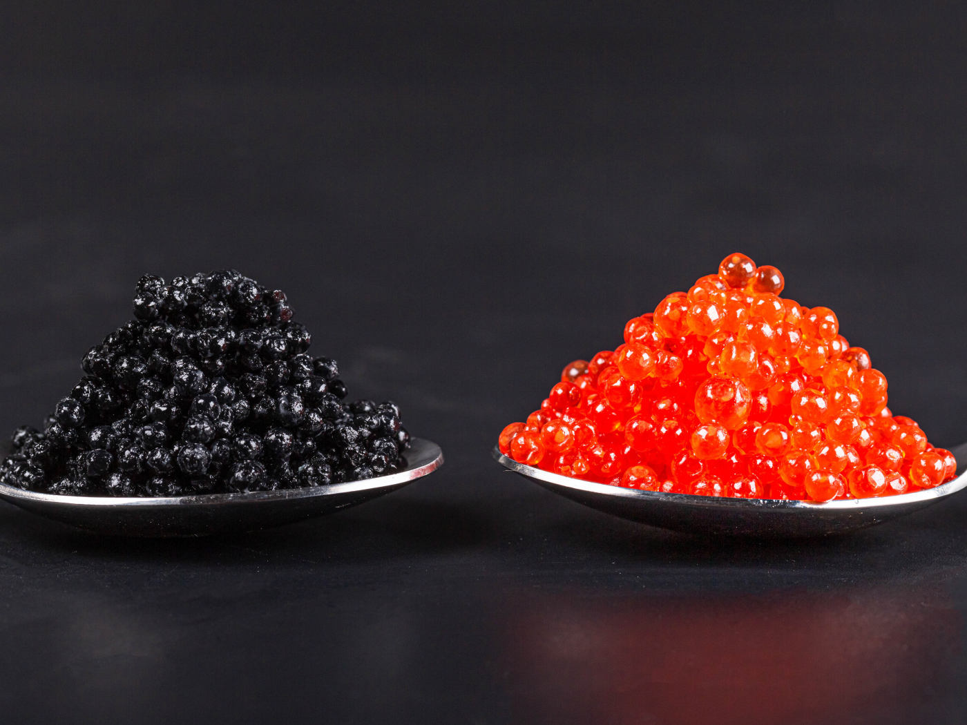 Красная и черная икра на ложках на сером фоне