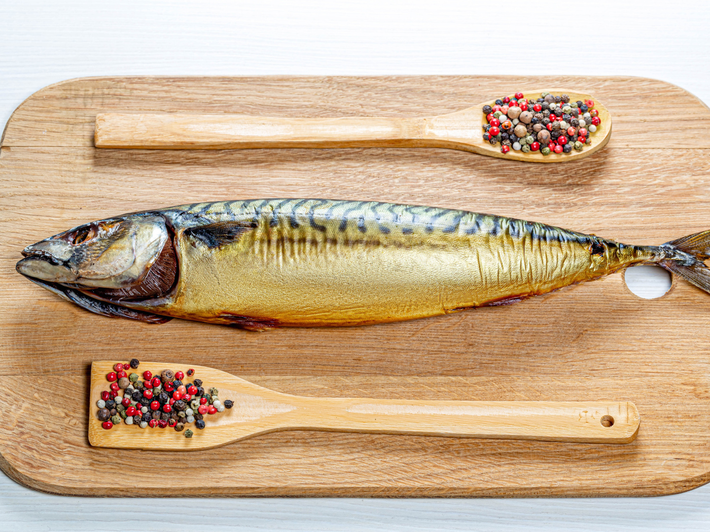 Копченая скумбрия на разделочной доске с перцем на белом фоне