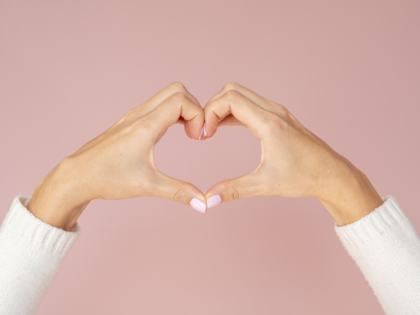 Girl making a heart with her hands on a pink background