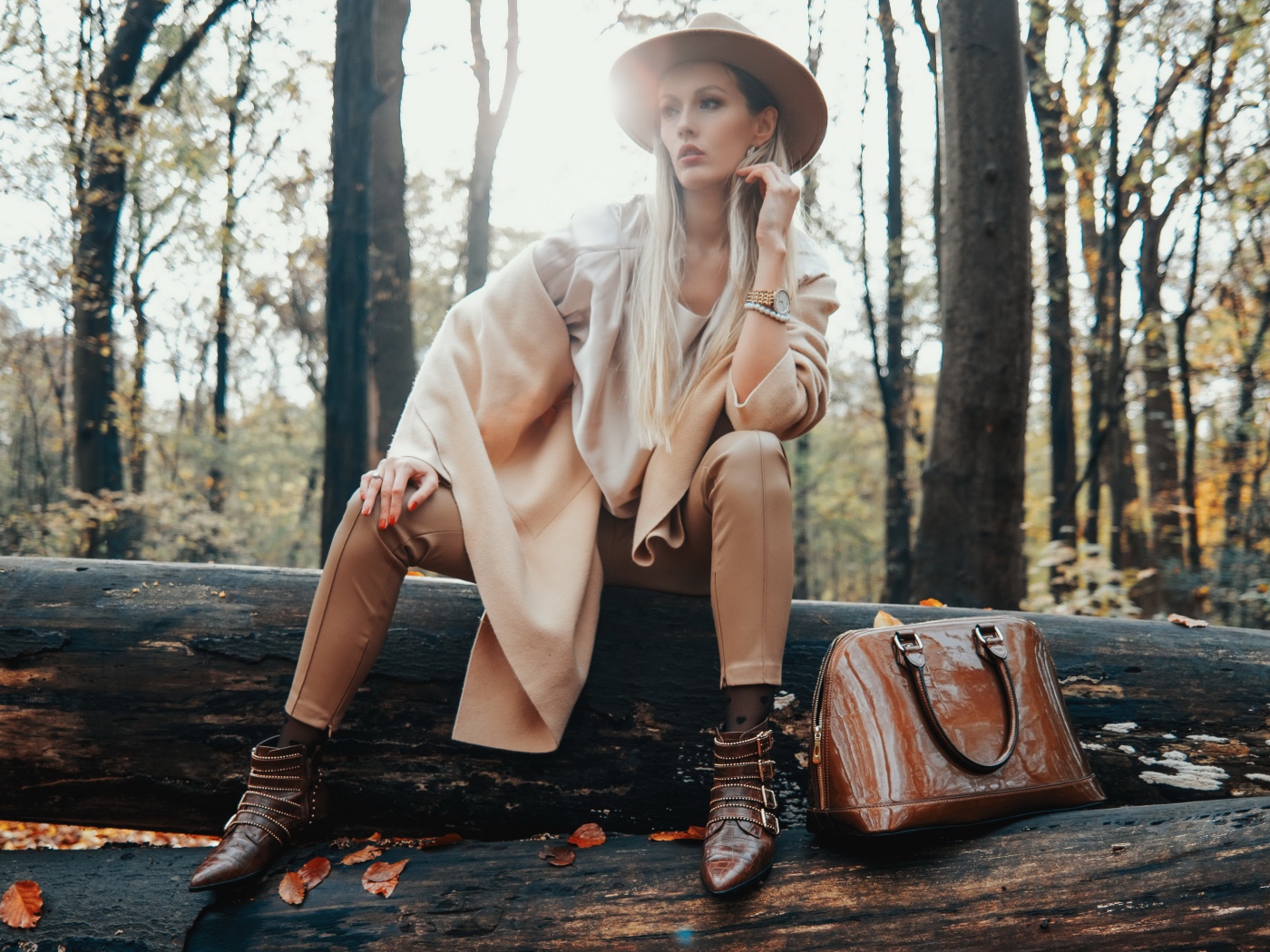 Девушка в пальто сидит на упавшем дереве в лесу 