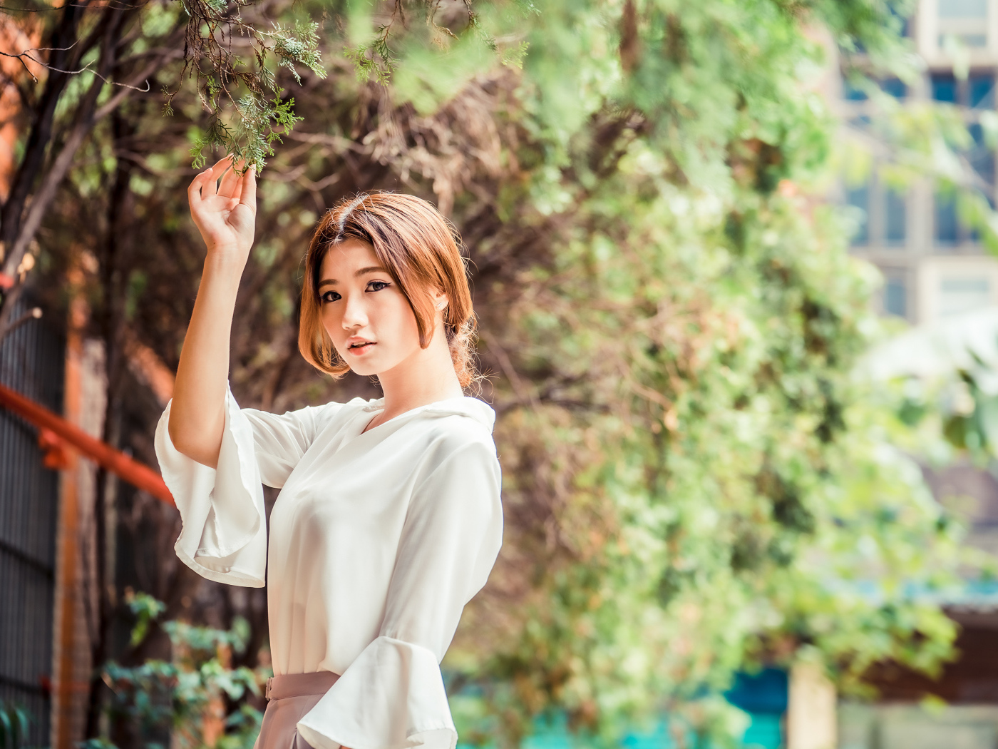Молодая азиатка в белой блузке стоит у дерева 