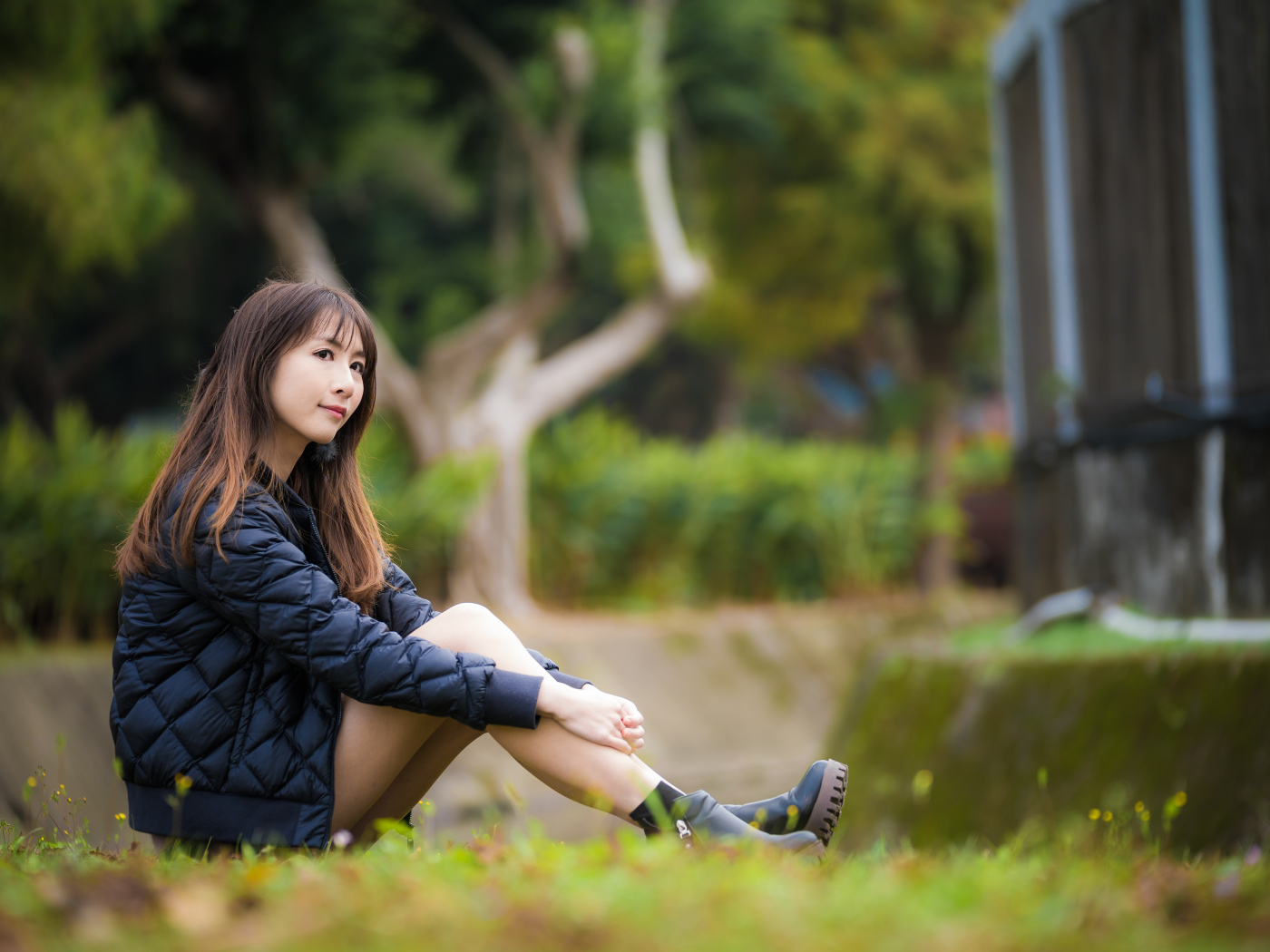 Девушка азиатка в черной куртке сидит на траве