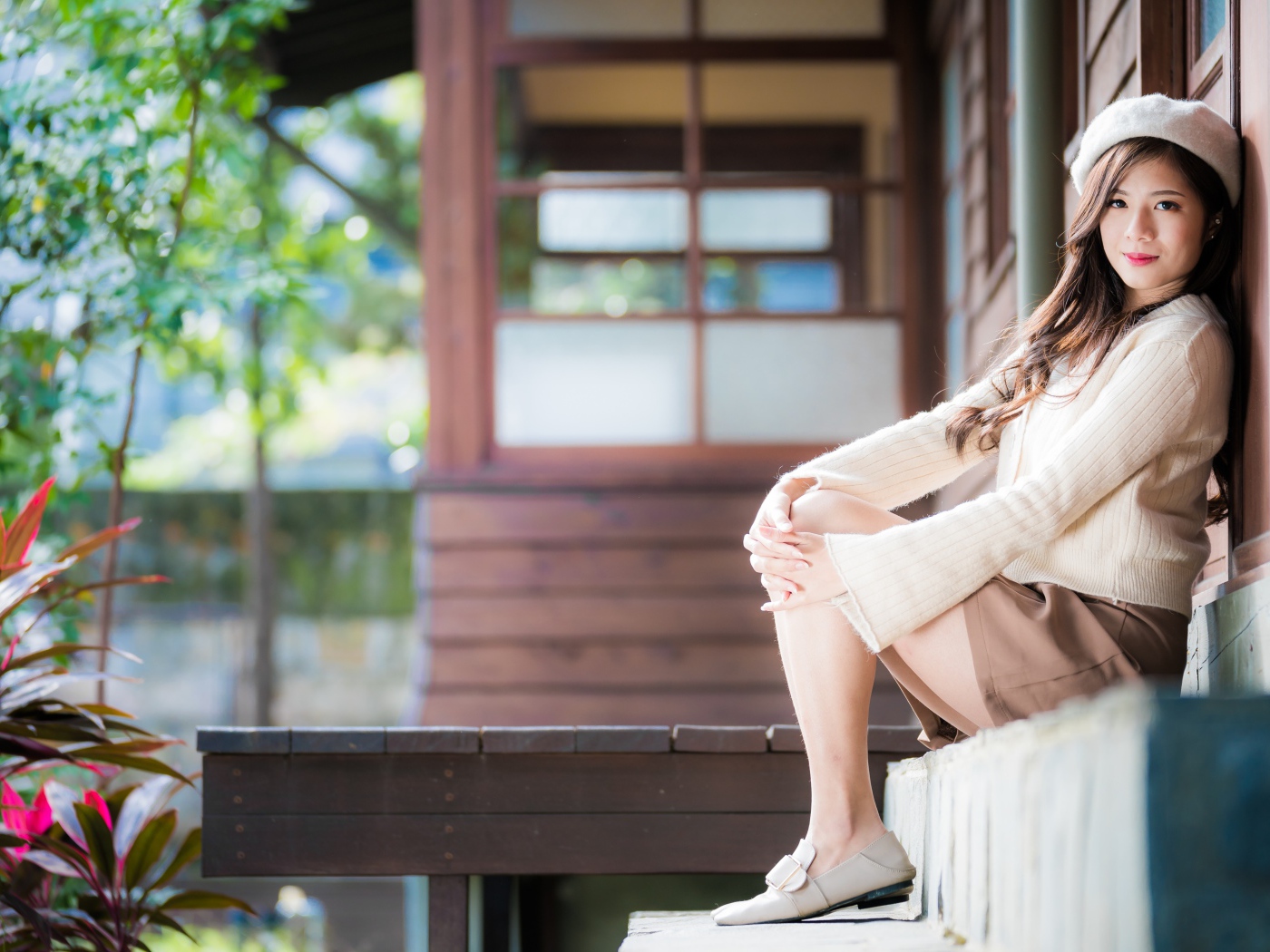 Девушка азиатка в свитере сидит на пороге 