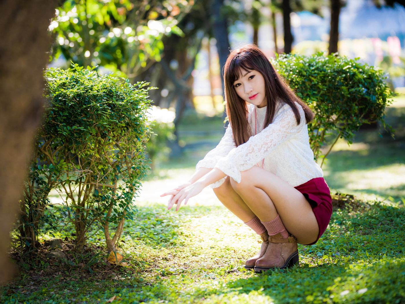 Девушка азиатка сидит на корточках в парке