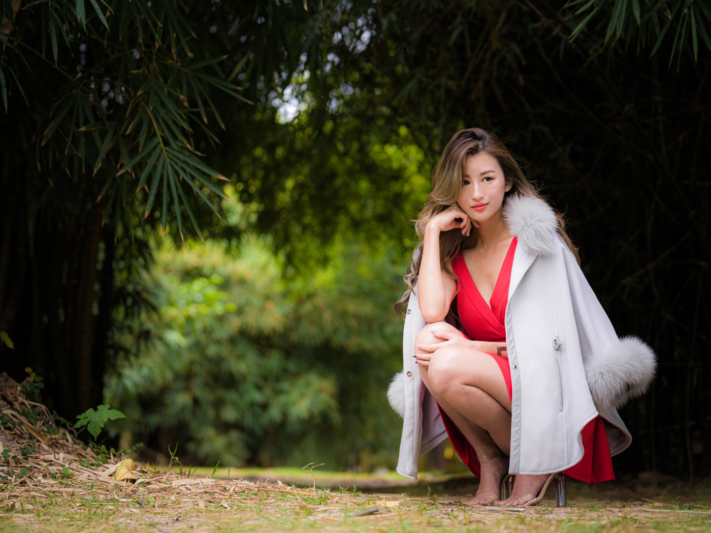 Азиатка в красном платье сидит в парке 