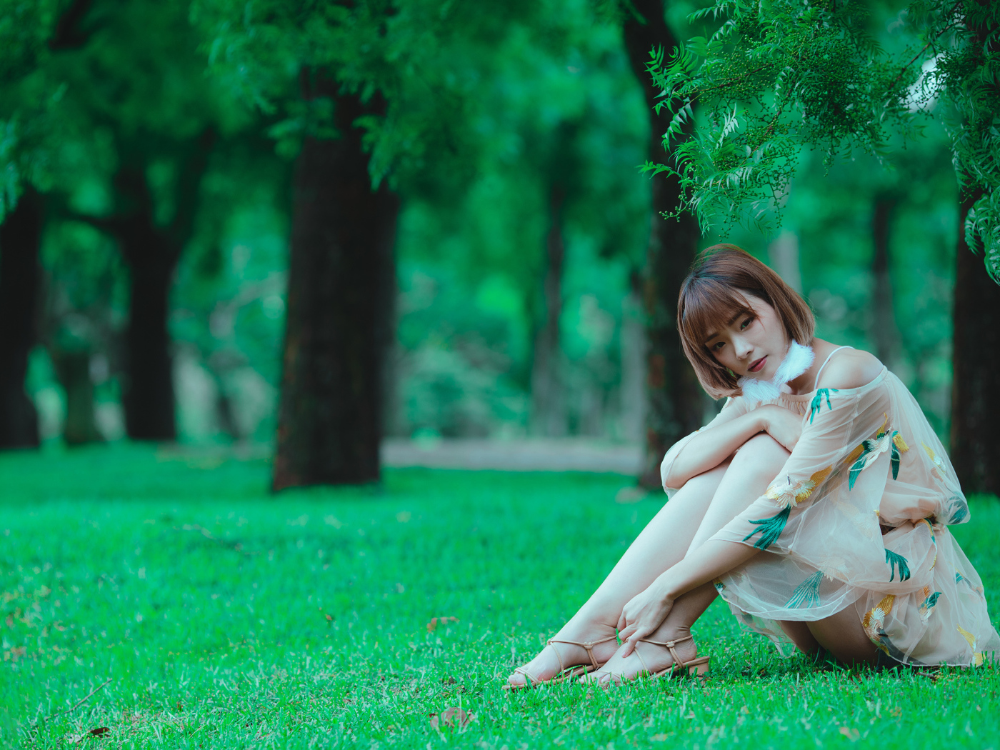 Красивая девушка азиатка сидит на зеленой траве в парке 