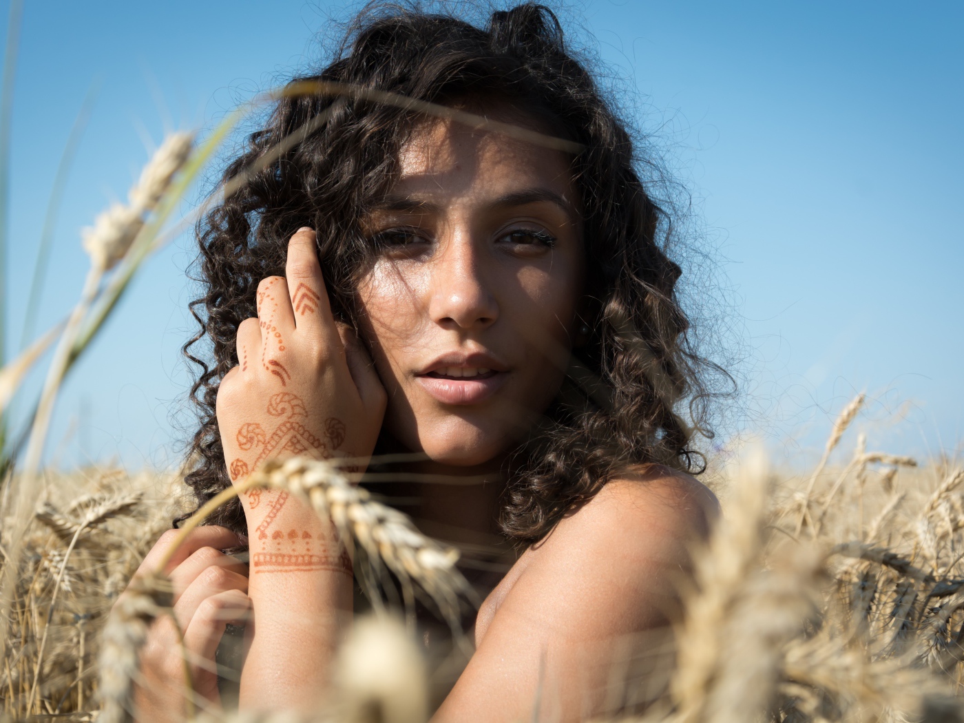 Красивая девушка с рисунком мехенди на руке на пшеничном поле 