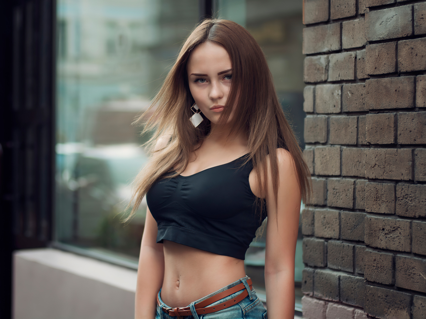 Красивая стройная девушка в черном топе стоит у стены