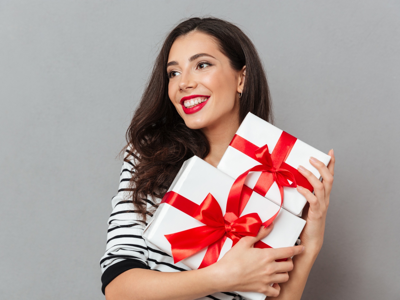 Красивая улыбающаяся девушка с подарками в руках на сером фоне 