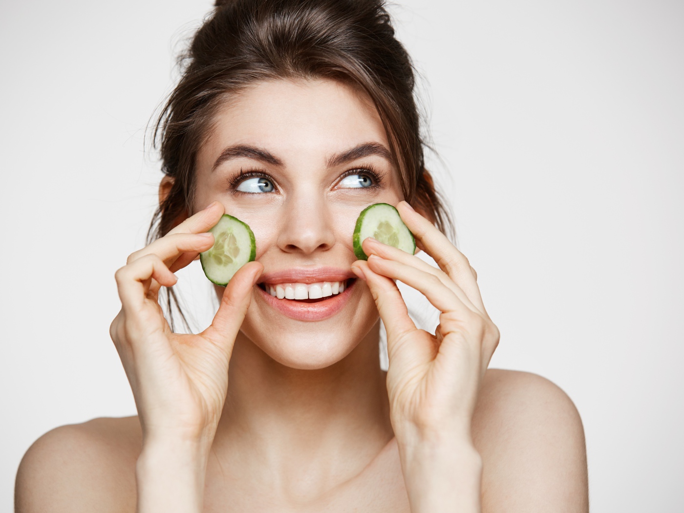 Голубоглазая девушка прикладывает огурцы к лицу 