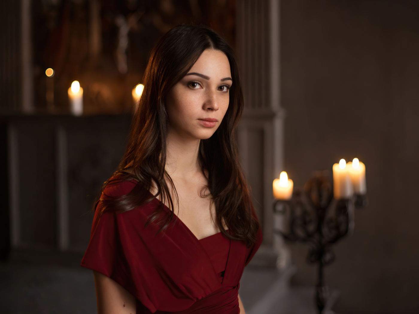 Кареглазая девушка в красном платье в комнате со свечами