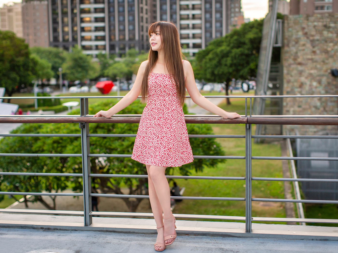 Милая девушка азиатка в платье стоит у перил 